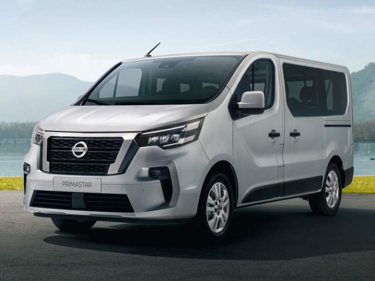 Furgone Nissan Primastar grigio argento con finestrini laterali, targa con scritta PRIMASTAR, parcheggiato davanti a un lago