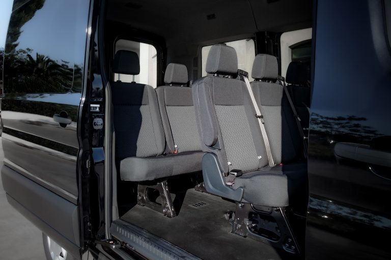 Interno di minibus nero con portellone scorrevole aperto, sedili in tessuto grigio con cinture e pianale scuro